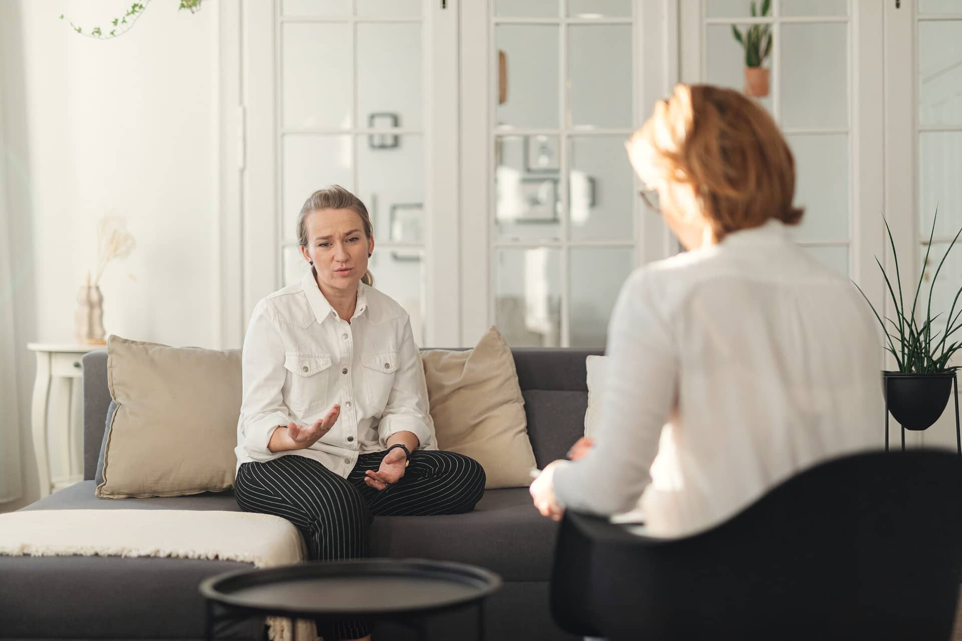 A therapist, seen from behind, listens as a client on a sofa talks through something.